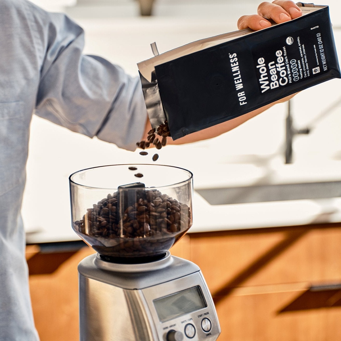 Person pouring whole coffee beans into a grinder.