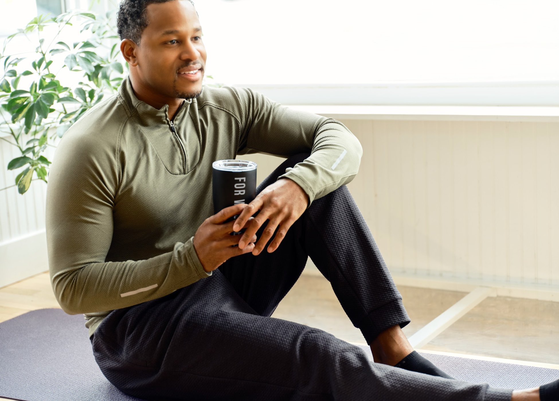 Man stretching while holding a For Wellness tumbler