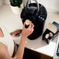 Person placing a coffee pod into a black coffee maker.