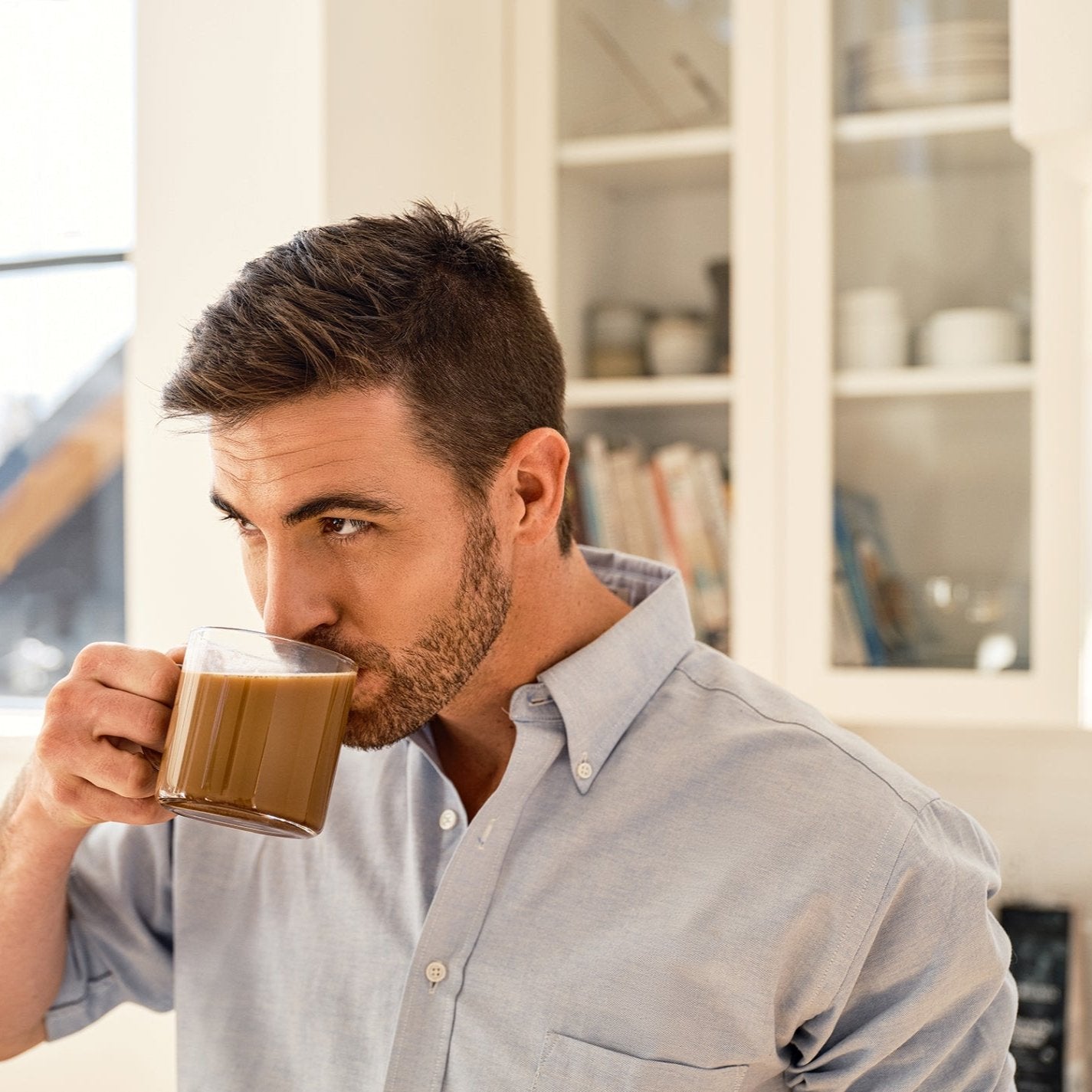 Man sipping coffee in a bright kitchen.