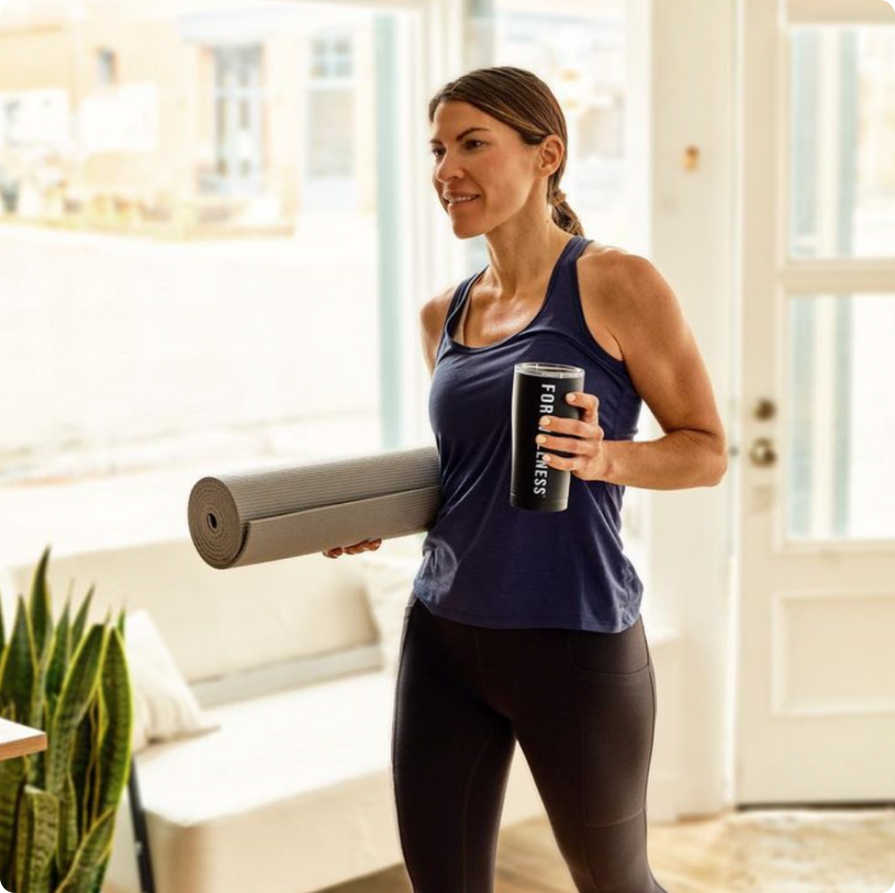 A woman holding a yoga mat and a For Wellness black tumbler 